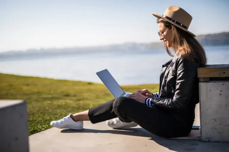 Imagem princial: Garota sentada no pier em frente a praia digitando no seu notebook